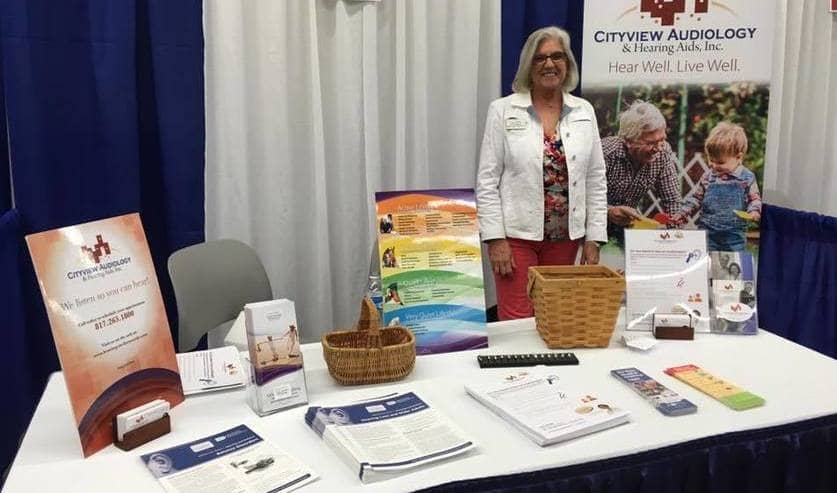 Professional standing behind a table full of business collateral at a trade fair.