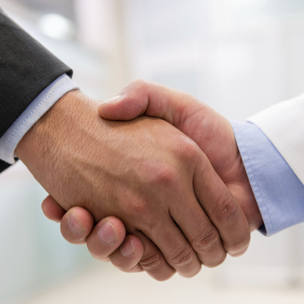 Two hands of what appear to be professionals, shaking hands as if making an agreement.