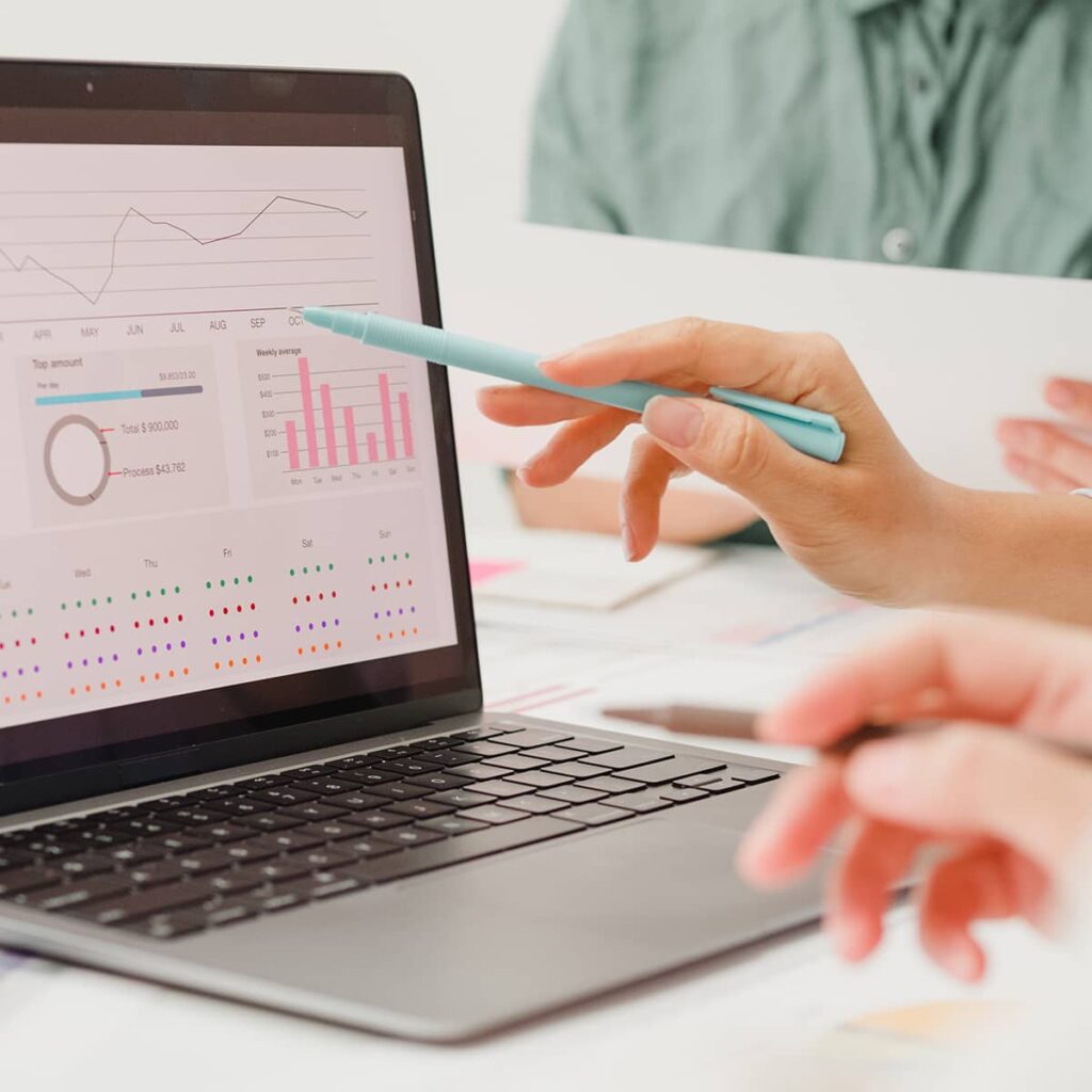 The hands of two professionals analyzing charts and graphs on a laptop screen.